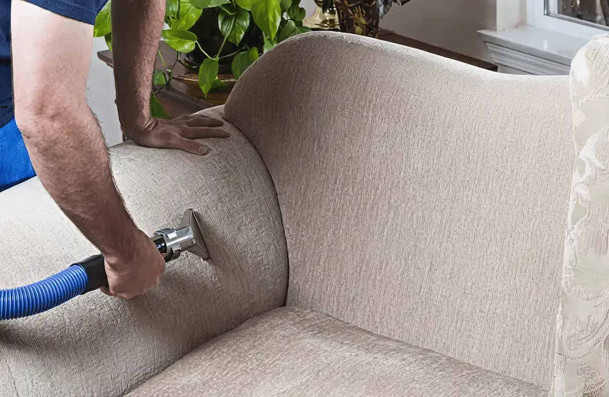 Professional upholstery cleaner deep-cleaning a fabric sofa with a handheld extraction tool and hose, Bloomington, IN.